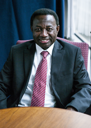 Image of John Abrefah wearing a blue suit jacket with white shirt and red tie